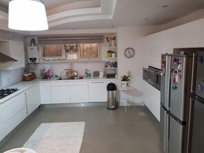 Una cucina moderna con mobili bianchi, un frigorifero in acciaio inossidabile e un piccolo tavolo bianco con una sveglia appesa al muro.