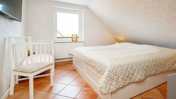 Een slaapkamer met een bed, een raam, een radiator en een stoel.