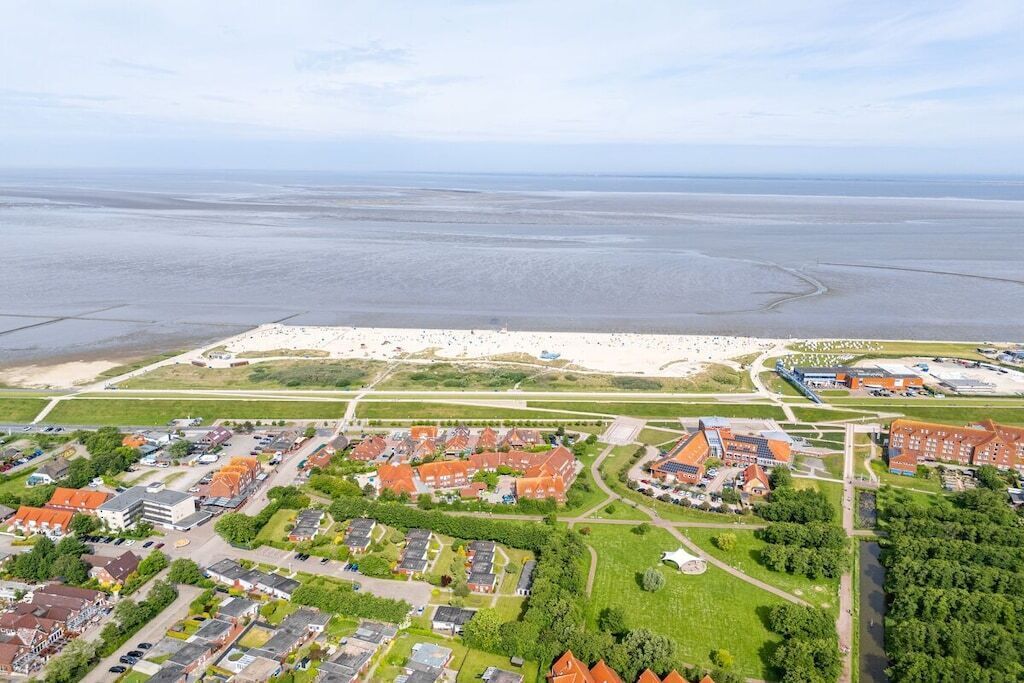 An aerial view of a coastal town with residential buildings, a sandy beach, and a large body of water.