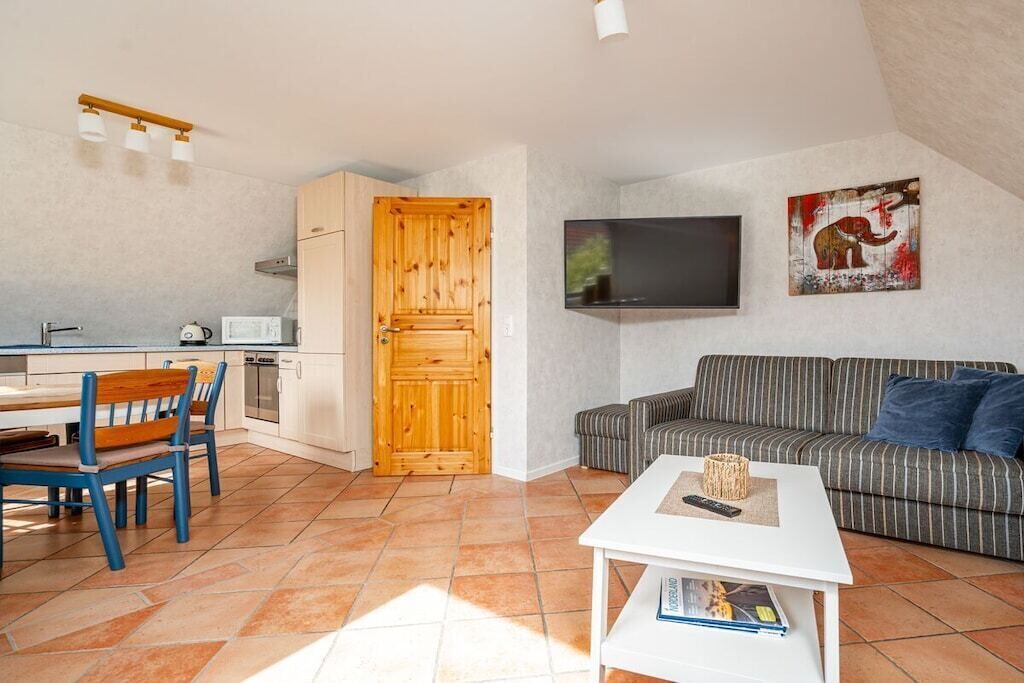 A compact living space with a kitchenette, a dining area with blue chairs, a striped sofa, a flat-screen TV, and a painting on the wall.