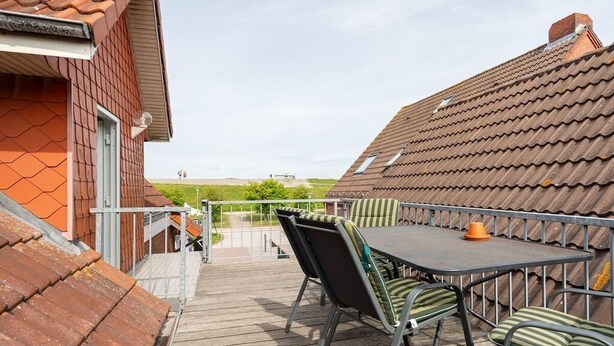 Um terraço com mesa e cadeiras, com vista para um campo gramado.