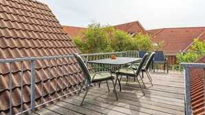 Um pátio externo com uma mesa e cadeiras, cercado por um guarda-corpo de metal.