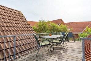 Une terrasse extérieure avec une table et des chaises, entourée d’une rambarde en métal.