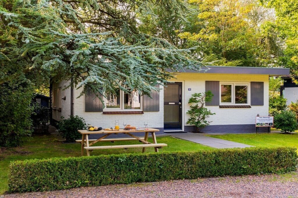 Un petit bâtiment d’un seul étage, à l’extérieur blanc et aux bordures sombres. Devant, on trouve une table de pique-nique en bois, avec de la nourriture et des boissons, ainsi qu’une pelouse bien entretenue.