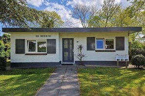 Een laag gebouw met een plat dak, een donkere voordeur en een klein raam aan de rechterkant.