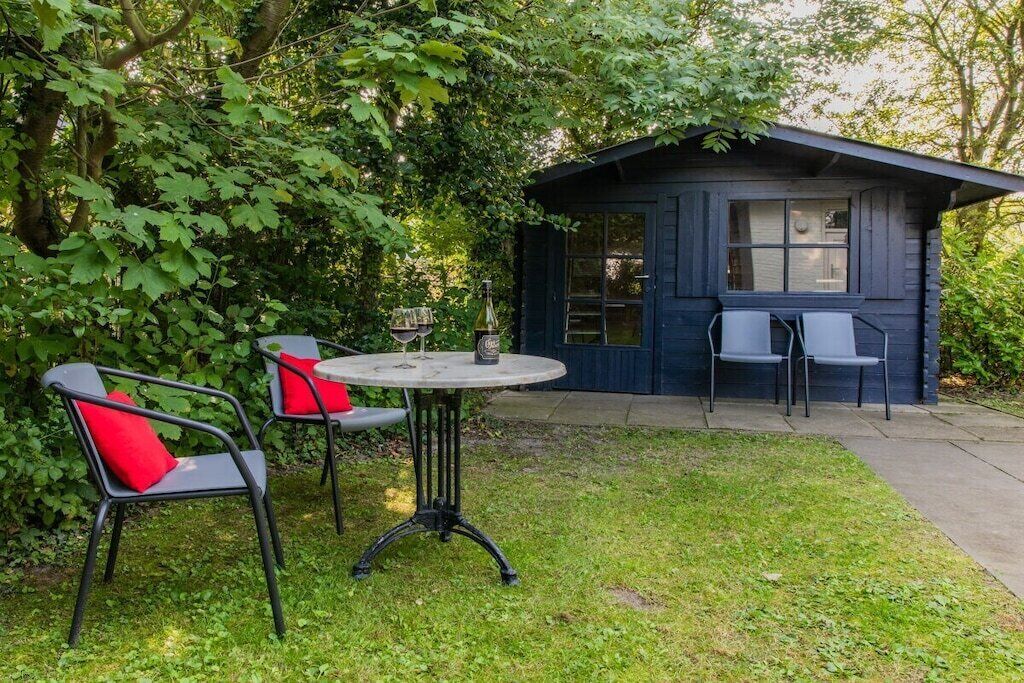 Uma pequena cabana de madeira com mesa e cadeiras em um jardim.