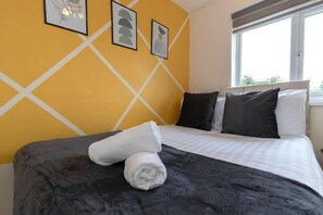A hotel room with a bed, pillows, a rolled towel, and artwork on the wall. - Spacious 2BR Home | Attic Room, Parking & WiFi (Sunderland)