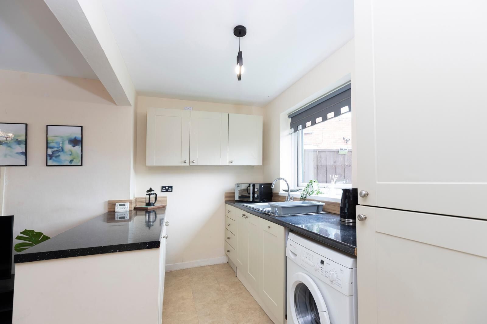 A compact kitchen with a washing machine, a sink, and a window with a view.