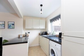 A compact kitchen with a washing machine, a sink, and a window with a view. - Spacious 2BR Home | Attic Room, Parking & WiFi (Sunderland)