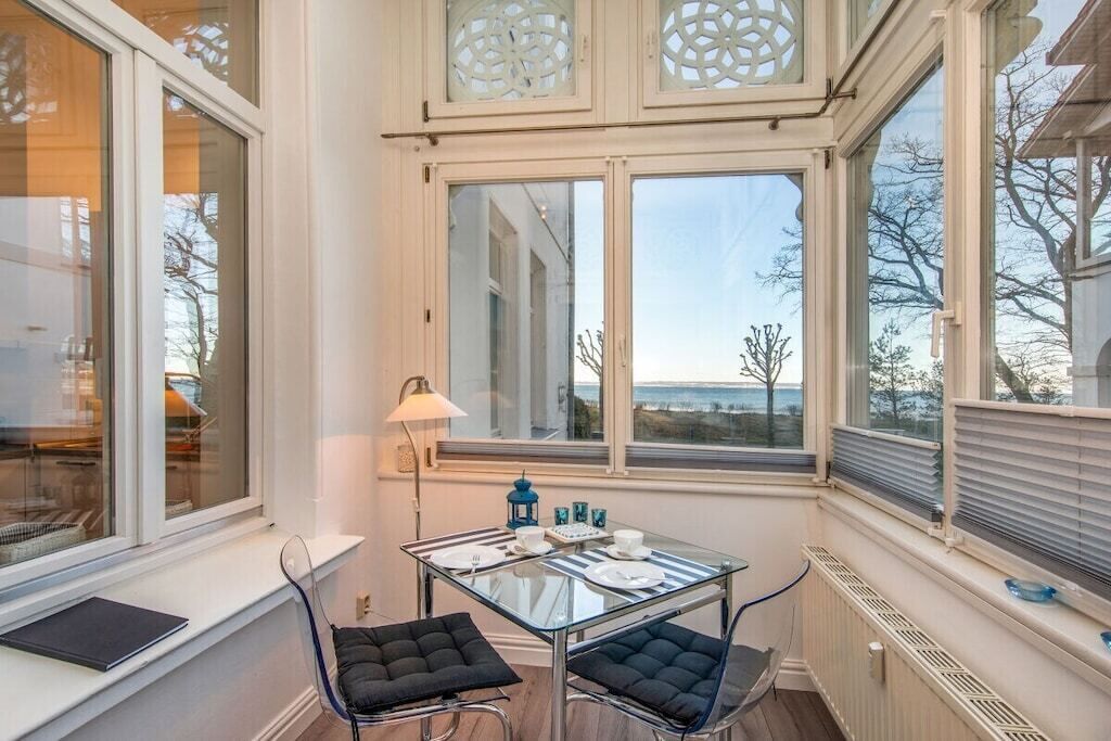 Et værelse med et glasbord, to stole, en lampe og udsigt gennem store vinduer.