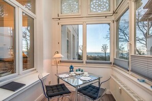 A room with a glass table, two chairs, a lamp, and a view through large windows. - Holiday apartment with 1 bedroom (Ostseebad Binz)