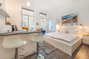 A modern bedroom with a bed, bedside tables, a desk with a chair, and a window. - Holiday apartment with 1 bedroom (Ostseebad Binz)