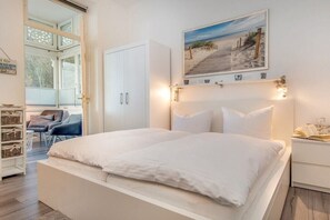 A bedroom with a bed, a nightstand, a window, and a painting on the wall. - Holiday apartment with 1 bedroom (Ostseebad Binz)