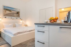 Een slaapkamer met een bed, nachtkastje, wandplank met decoratieve objecten en een fruitschaal op het dressoir.