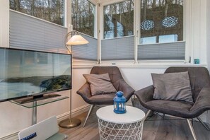 Un salon moderne doté d’un téléviseur à écran plat, de deux fauteuils en cuir, d’une table basse ronde et d’un lampadaire.