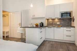 A compact kitchen with white cabinetry, a built-in oven, and a countertop with a kettle and coffee maker. - Holiday apartment with 1 bedroom (Ostseebad Binz)