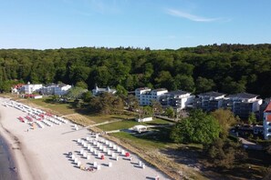 A coastal hotel with multiple buildings, a sandy beach, and a forested hill in the background. - Holiday apartment with 1 bedroom (Ostseebad Binz)