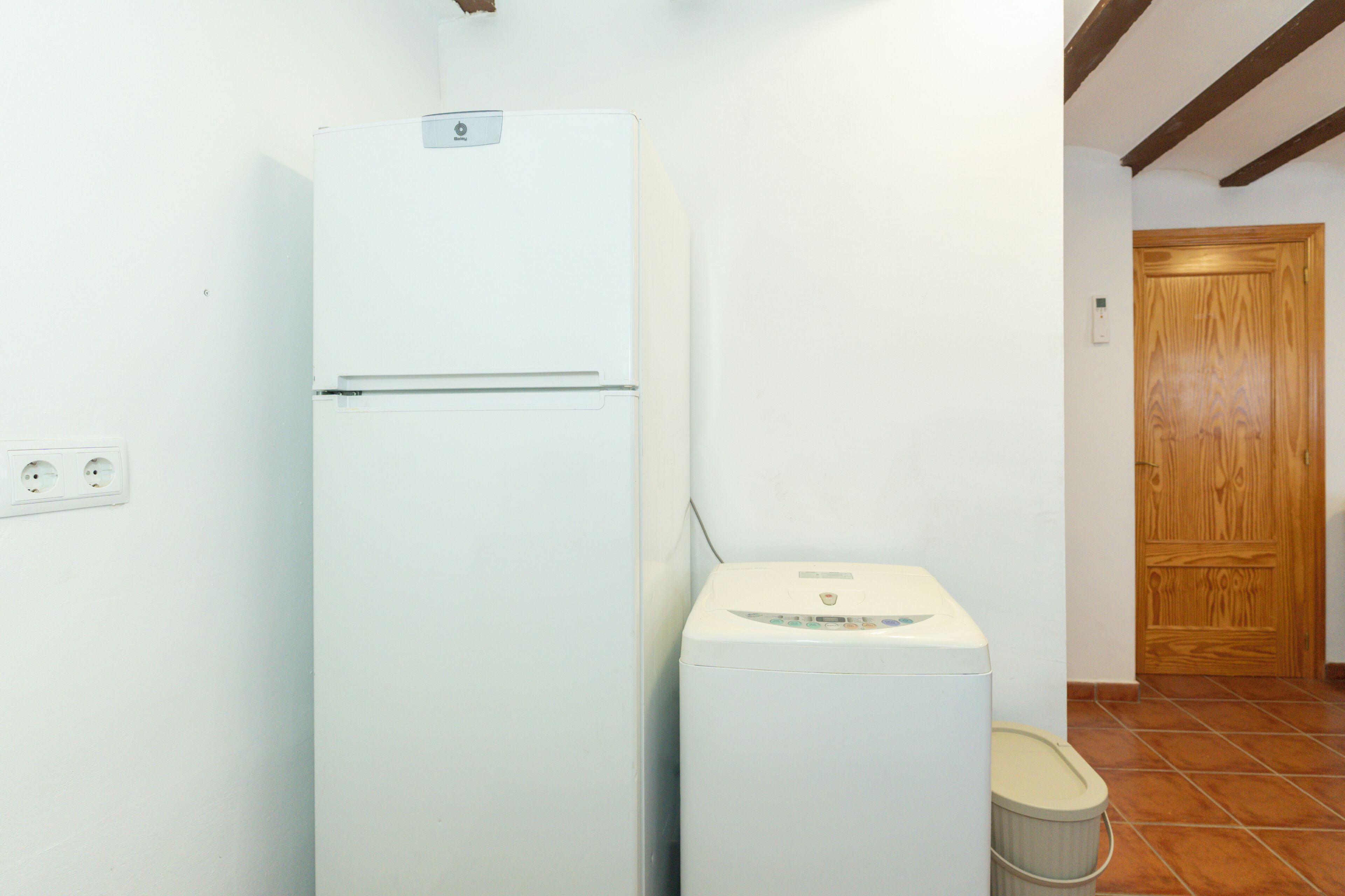 Eine kleine Küche mit einem weißen Kühlschrank, einer Waschmaschine und einer Holztür.