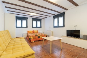 A small, furnished room with a sofa, a bed with a quilt, a television, and a radiator. - Paramera Apartment (Blancas)