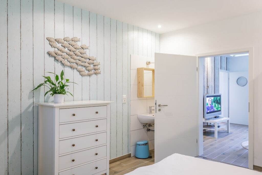 A bedroom with a bed, a dresser, a wall-mounted plant, a television, and a bathroom with a sink and mirror.