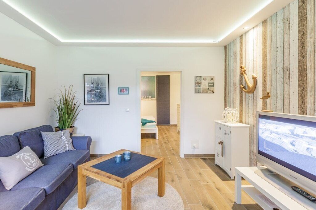 Un salon moderne avec un canapé, une table basse et un téléviseur. Le sol est en bois et il y a une plante dans un coin.
