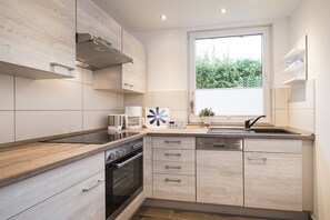 A modern kitchen with light wood cabinetry, a built-in oven, and a window with a view of greenery. - Bungalow in Travemünde with swimming pool (Travemünde)
