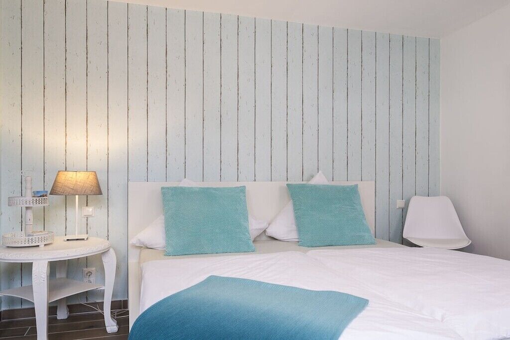 Une chambre d’hôtel avec un lit, deux oreillers, une table de chevet avec une lampe et un mur orné de lignes verticales.