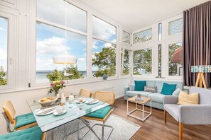 A spacious room with a dining table set for two, a sofa, and a view of the outdoors. - Vista Mare at Villa Agnes (Binz)