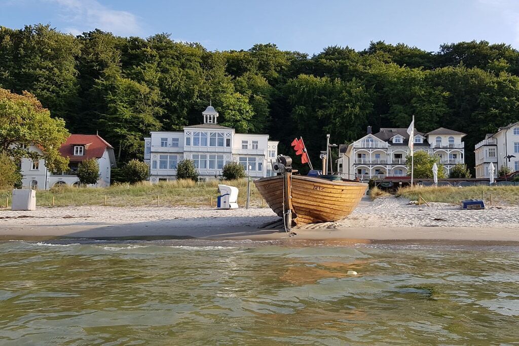 A wooden boat on a sandy beach with buildings in the background.
