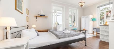 Ein modernes Schlafzimmer mit einem Bett, Nachttischen, einer Hängeleuchte und Blick ins Freie.