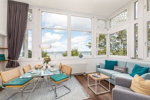 A room with a dining table, chairs, a sofa, and a view of the sea. - Vista Mare at Villa Agnes (Binz)