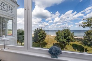 Een kamer met een groot raam met uitzicht op een strand, een witte decoratie op de vensterbank, en een klein visje versierd.