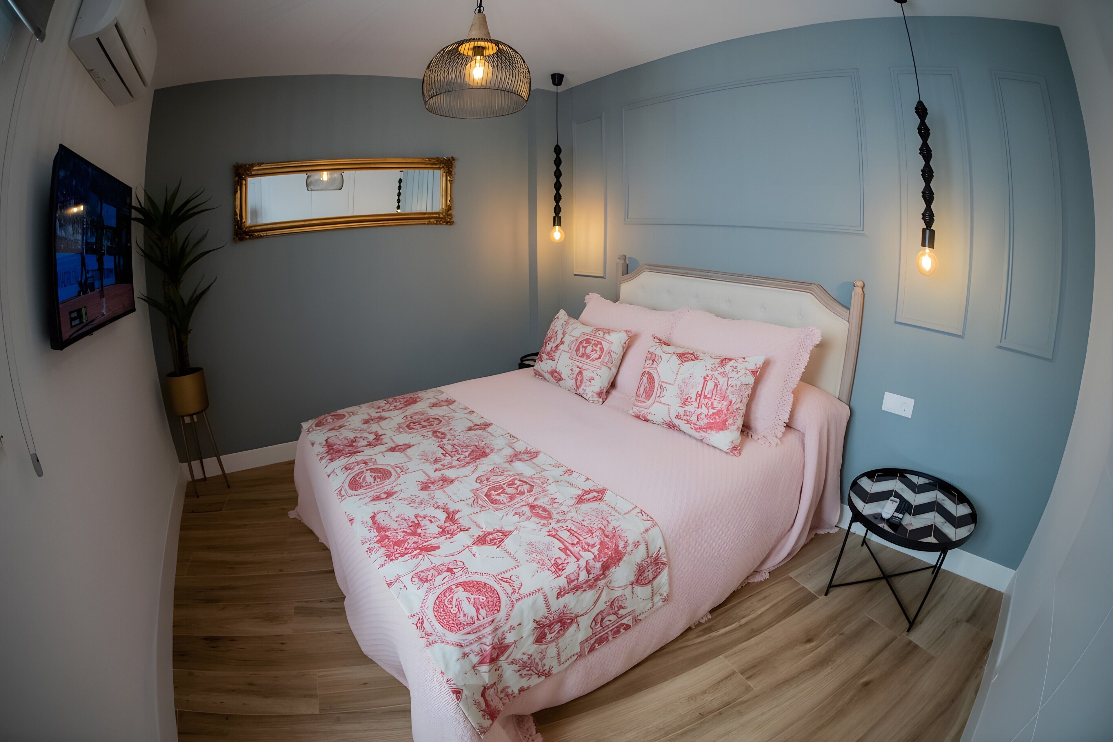 Une chambre à coucher avec un lit, un miroir, un luminaire suspendu et une petite table.