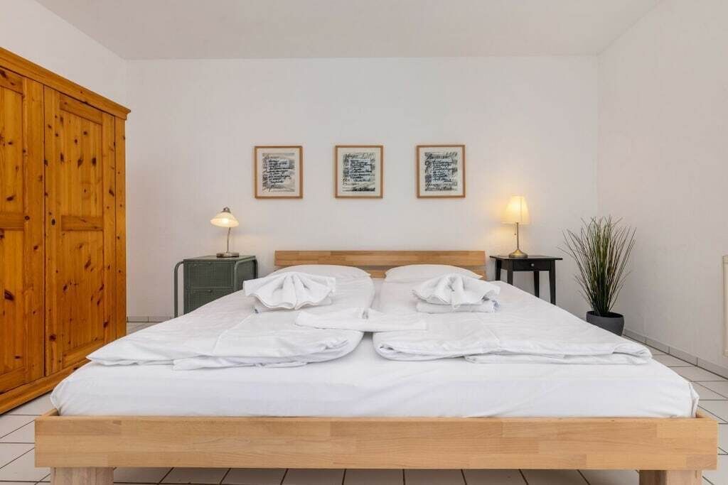 Un lit bien fait, avec des draps blancs, une tête de lit en bois et trois tableaux encadrés accrochés au mur.
