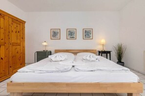 Ein ordentlich bezogenes Bett mit weißen Leinen, einem hölzernen Kopfteil und drei gerahmten Objekten an der Wand.