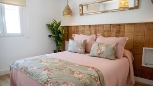 Una camera da letto con testiera in legno, un letto con lenzuola a motivi floreali, una pianta in vaso e un comodino con una lampada.