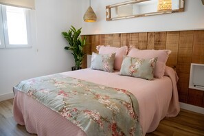 Ein Schlafzimmer mit einem hölzernen Kopfteil, einem Bett mit floralem Bettbezug, einer Zimmerpflanze und einem Nachttisch mit einer Lampe.
