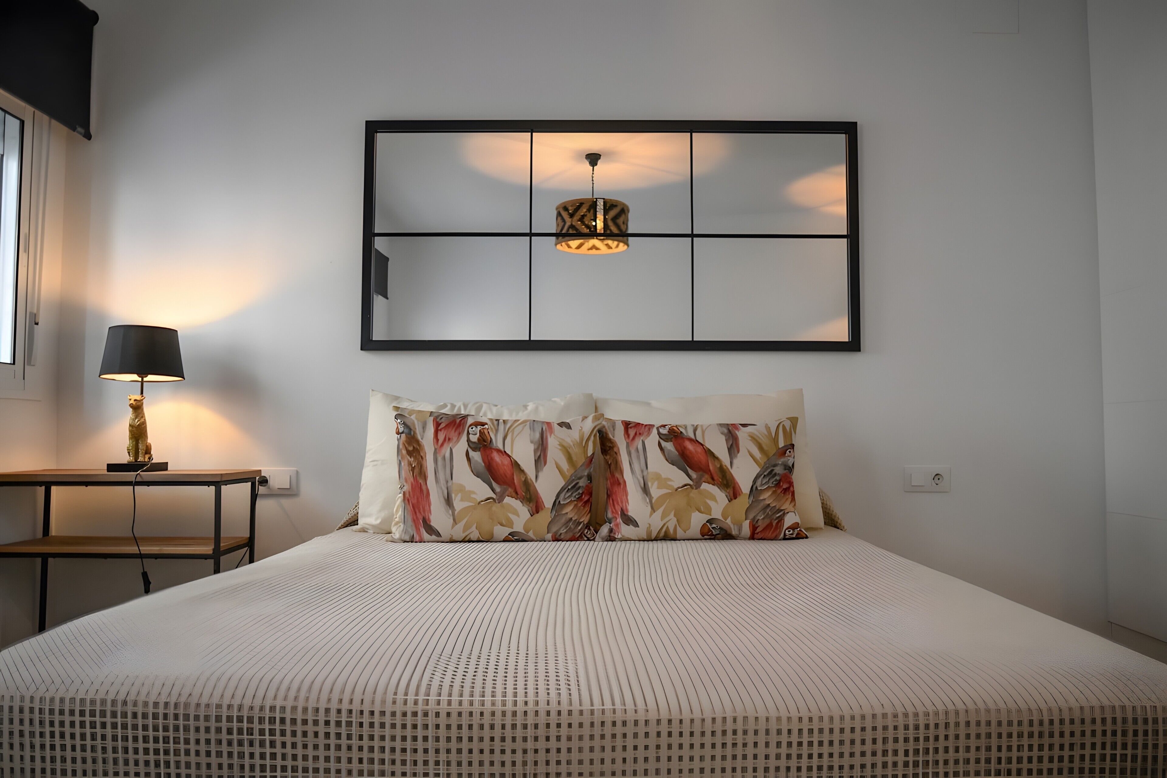 Ein Schlafzimmer mit einem Bett, einem Nachttisch, einer Lampe, einer Wandleuchte und einem gerahmten Kunstwerk über dem Bett.