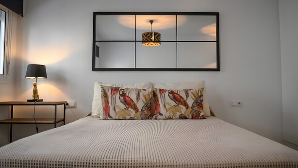 Una camera da letto con un letto, un comodino, una lampada, un punto luce a parete e un quadro appeso sopra il letto.