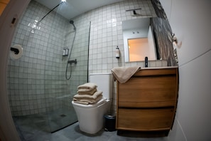 A modern bathroom with a glass-enclosed shower, a toilet, and a wooden vanity with a towel stack. - Studio Apartment No.2 – Comfort and Style in El Puerto de Santa María (El Puerto de Santa María)