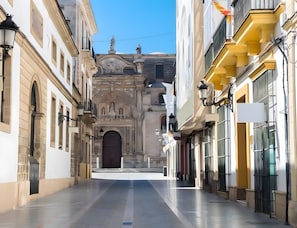 A narrow street with buildings on either side, a large ornate entrance, and a clear sky. - Studio Apartment No.2 – Comfort and Style in El Puerto de Santa María (El Puerto de Santa María)