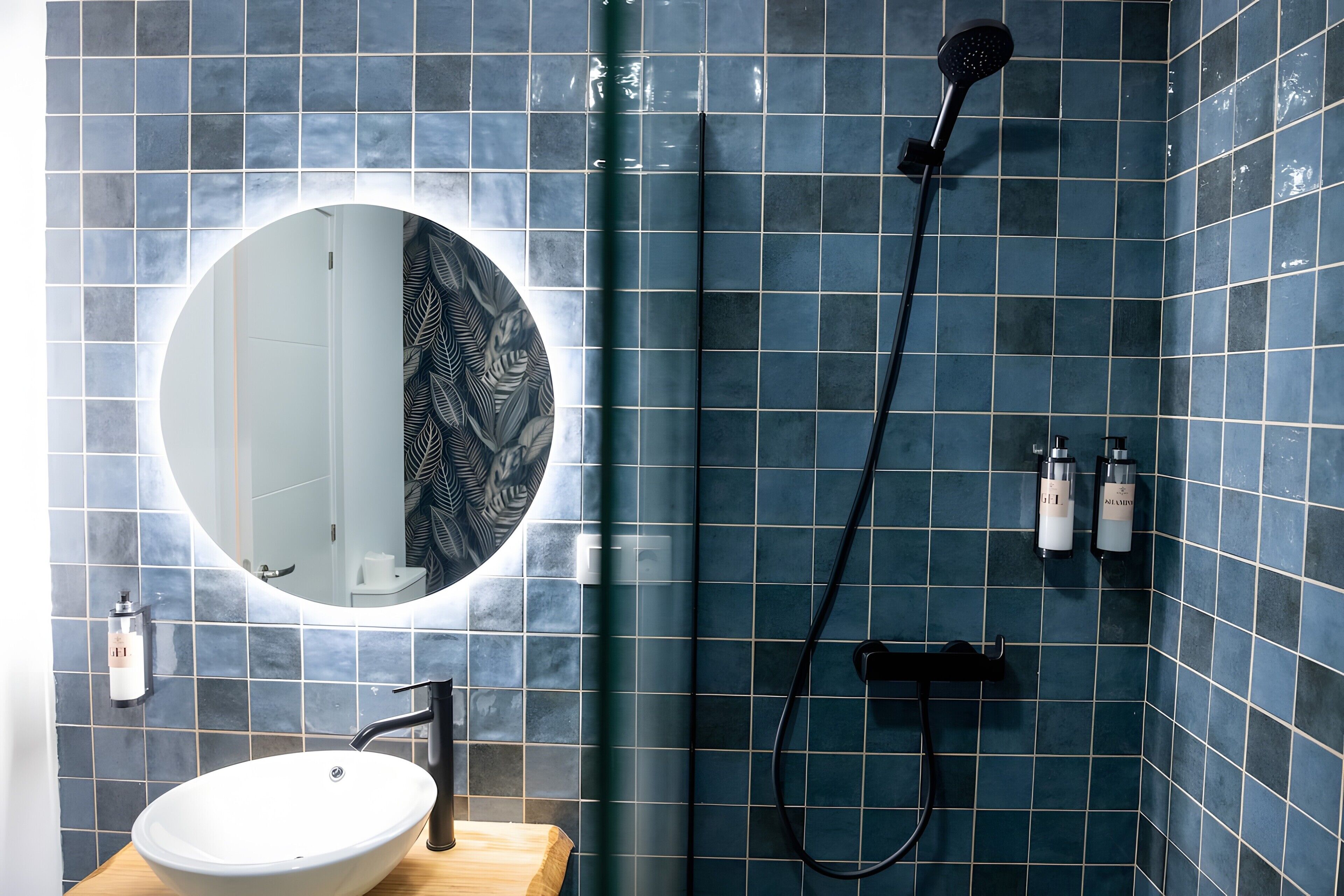Ein Badezimmer mit einem runden Spiegel, einem weißen Waschbecken und einer Duschkabine mit Duschbrause.