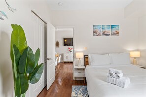 A hotel room with a bed, bedside lamps, a large plant, and a view of the hallway.