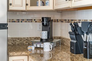 A kitchen with a coffee maker, two mugs, a knife block, and a tiled backsplash.