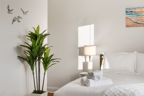 Habitación de hotel con una cama, una lámpara de noche, una planta y un cuadro de una playa.