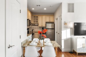 Una cocina moderna con armarios blancos, encimera de granito y una mesa de comedor preparada para cuatro personas.