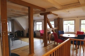 A room with a wooden staircase, a dining table with chairs, and large windows. - Holiday apartment with 1 bedroom (Sankt Andreasberg)