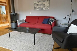 A living room with a red sofa, a black armchair, a glass coffee table, and a wood-burning stove. - Holiday apartment with 1 bedroom (Sankt Andreasberg)