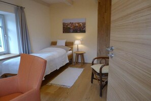 Habitació d'hotel amb un llit, una cadira, una taula petita, una làmpada i un quadre a la paret.