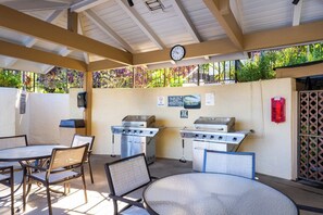 Un patio al aire libre con una parrilla, mesas, sillas y un reloj en la pared.